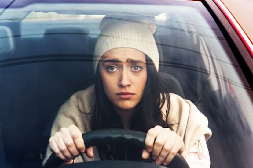 A confused mom in a beige jacket and a beige hat driving a car  