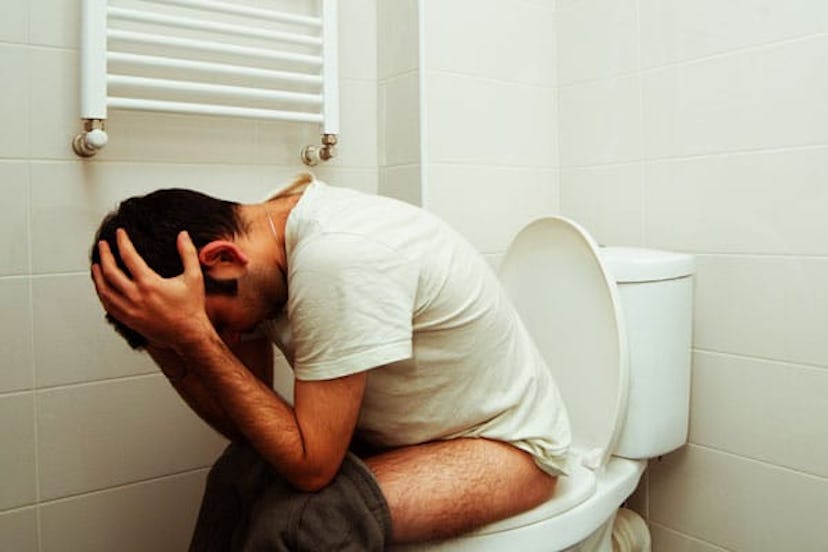 Man sitting on a toilet, holding his head, looking down