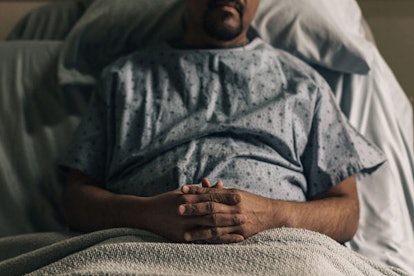 A man with brain cancer in a hospital gown lying in a hospital bed with his hand crossed on his lap