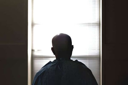 A man with brain cancer in hospital gown looking through the window