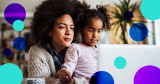 A curly black-haired woman in a beige sweater and her daughter sitting in her lap, both looking into...