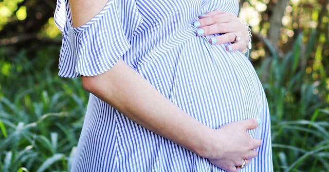 A pregnant woman in a blue-white off-the-shoulder striped dress with her hand on her belly