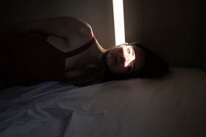 A woman lying in bed in a dark room with a streak of light over her face