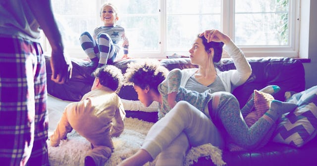 Mom sitting on a couch and her three little kids jumping around her and her husband