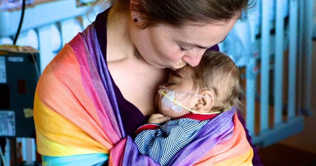 A mother holding her son who has feeding tubes attached to his face while they're both wrapped in a ...
