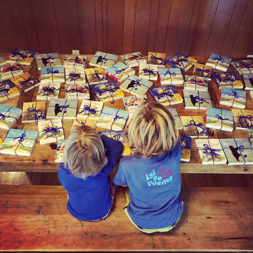 Two blonde boys sitting at a wooden bench with various books with blue ribbons placed on it
