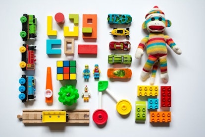 Lego bricks in various shapes, toy cars, and a knitted monkey toy placed on a white surface