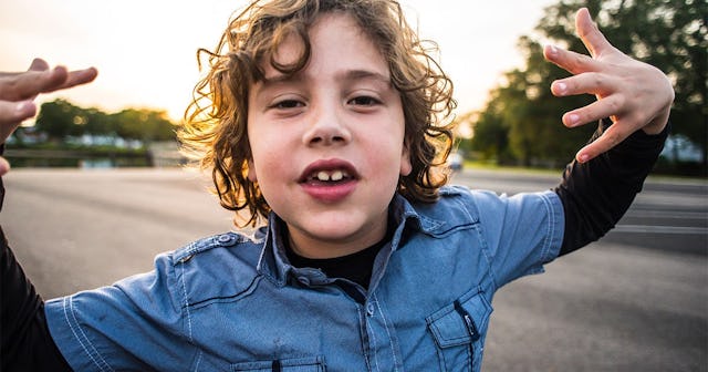 A kid bully making hand gestures at the camera while standing out in the road