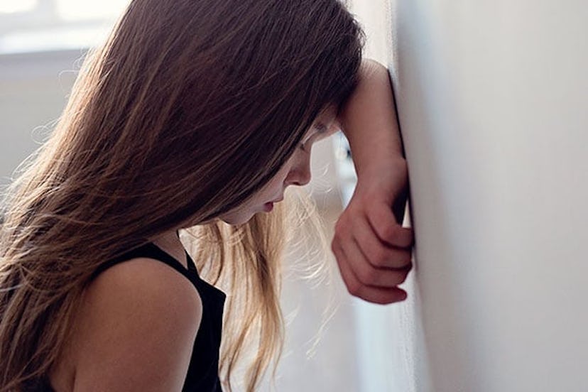 A girl sad after being bullied standing against the wall with her head resting on her arm