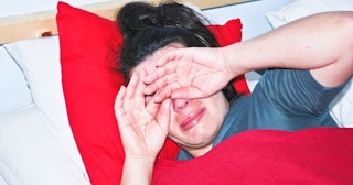 A woman crying in bed, hiding her face with her hands because of her miscarriage