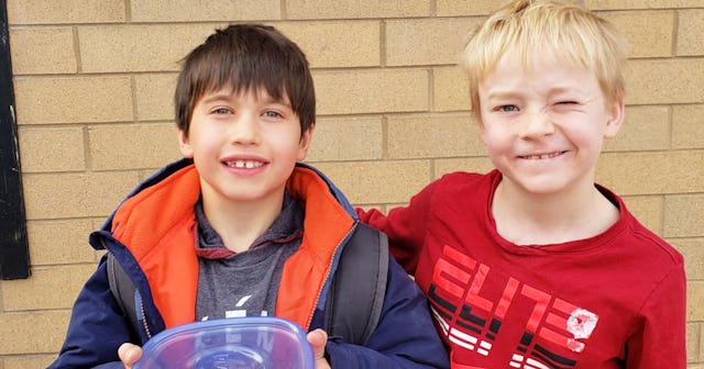 A brown-haired boy in a blue-orange jacket and a blonde boy in a red shirt dropping off cookies arou...