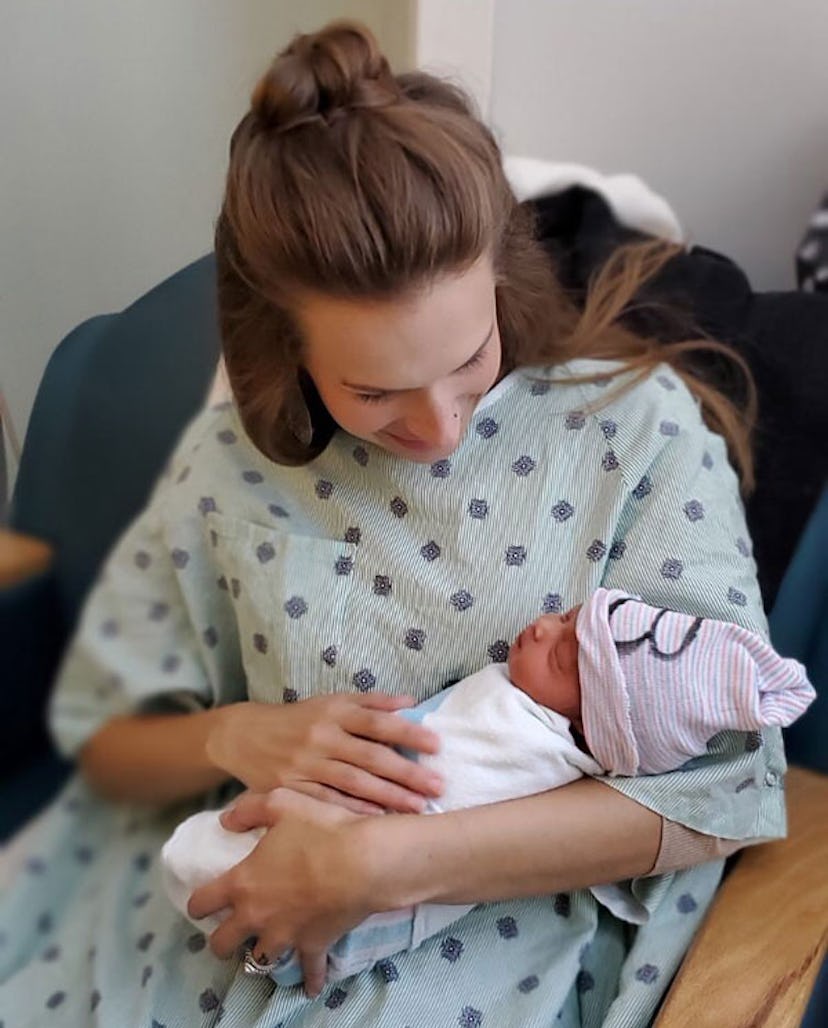 A mother in a blue hospital gown holding a newborn baby and looking at it