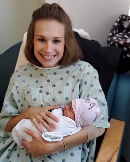A smiling mother in a blue hospital gown with a newborn baby 