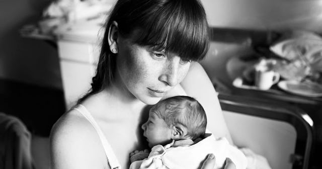 A dark-haired woman with bangs and a tank top holding her newborn baby on her chest in black and whi...