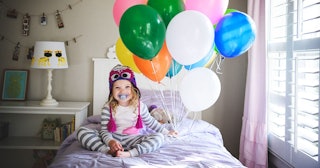 Little girl holding balloons while sitting on a bed 