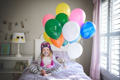 Baby girl sitting on a bed and holding many balloons