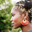 A profile of a woman with yellow and brown braids on her head and with an orange earring.