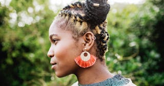 A profile of a woman with yellow and brown braids on her head and with an orange earring.