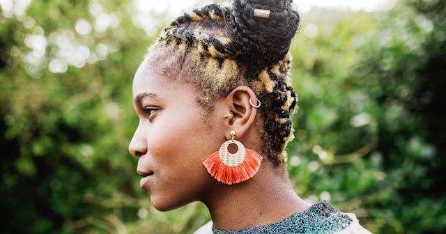 A profile of a woman with yellow and brown braids on her head and with an orange earring.
