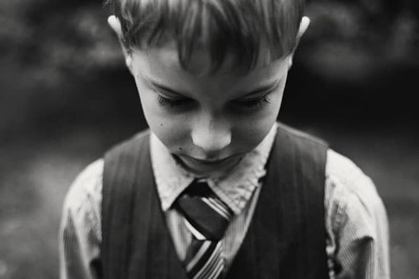 A boy in a shirt, waistcoat and tie looking down in black and white