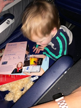A toddler playing with airplane brochures on his seat