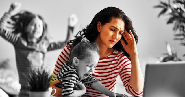 A stressed-out working mom holding a baby while her tween daughter is jumping in the background tryi...