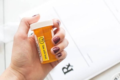 A woman's hand holding a prescription pill bottle with a "take with food" warning label.