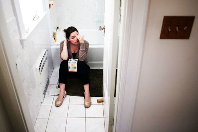 A pregnant woman sitting in the bathroom feeling nauseous and leaning against the bathtub 