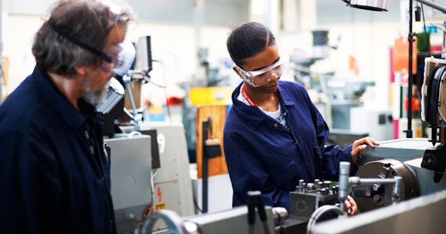Lecturer teaching student to operate machine in workshop