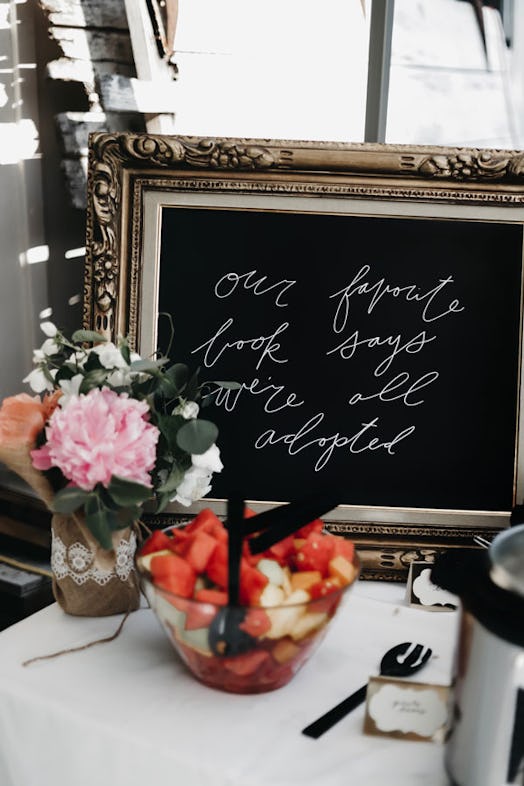 Table with flowers, fruit salad, and framed chalkboard reading 'Our favorite book says we're all ado...