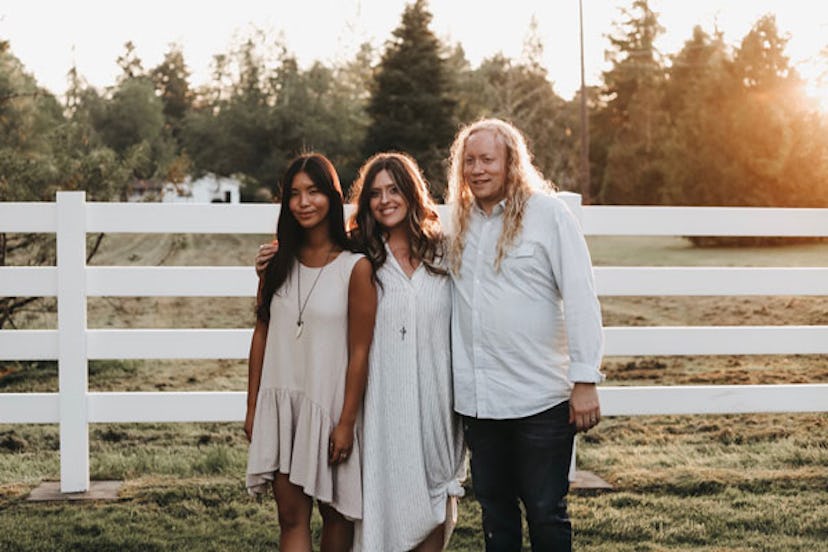 A couple with their adopted adult daughter posing and smiling while dressed in white on a ranch