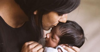 Black-haired mother holding and kissing her baby on the forehead 