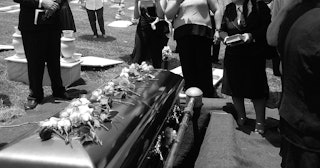 A funeral for an estranged grandma in a casket and people in black around it
