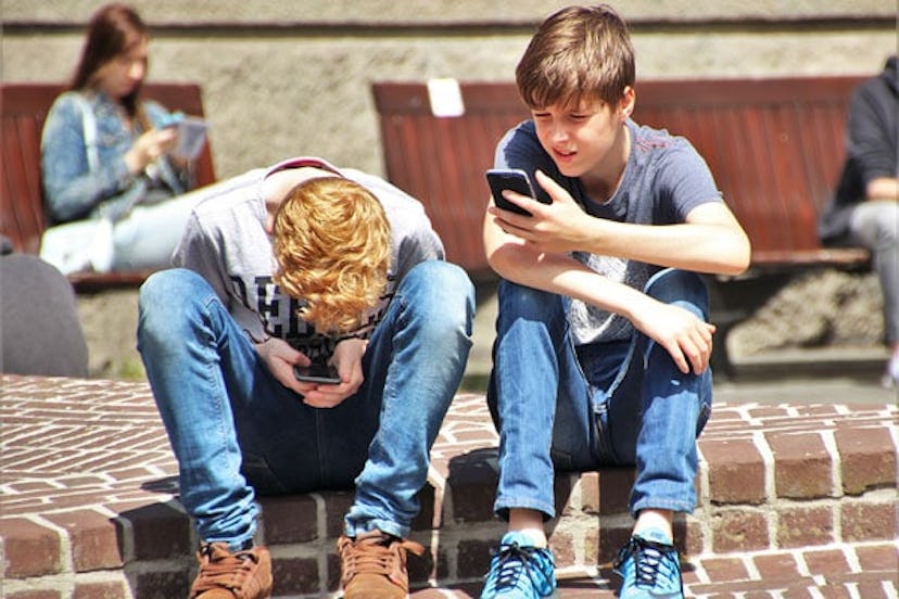 2 Boy Sitting on Brown Floor While Using Their Smartphone Near Woman Siiting on Bench Using Smartpho...