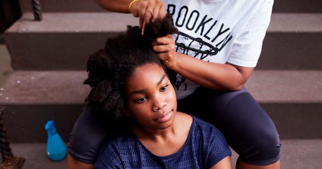 A mother makes the hair for her almost-teen daughter while they're sitting on steps