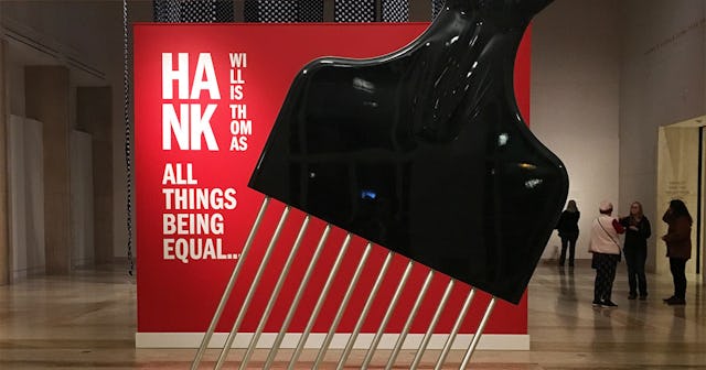 A red poster for the exhibition of Hank Willis Thomas behind an oversized black Afro pick comb