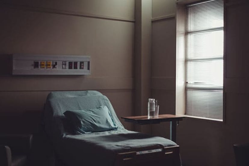 A hospital bed with blue bed sheets placed next to a window in a hospital room