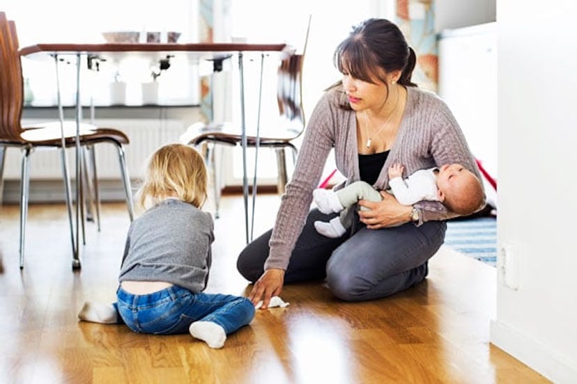Mother cleaning floor with daughter while holding baby at home