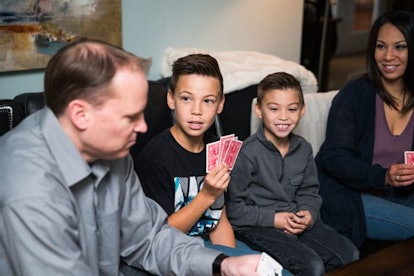 A family of a mother, father, and two boys play a game of cards while sitting on the same couch. The...