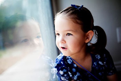ittle girl in blue looking out a window and smiling