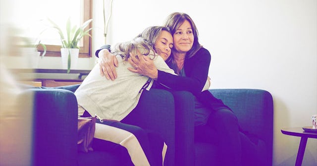 Mother and daughter embracing while sitting on couch