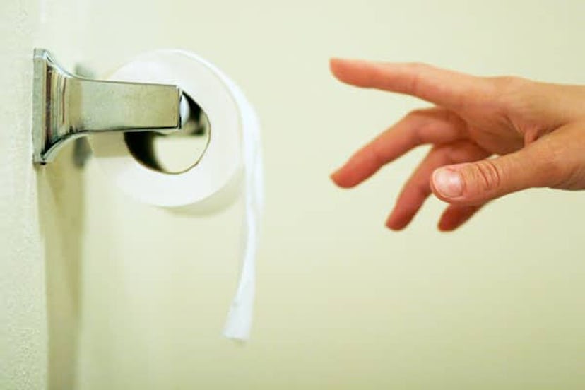 A female hand reaching to pull toilet paper off the roll.