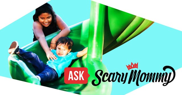 Older sister helping her younger brother go down a twisted slide in a kids playground.