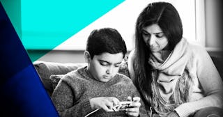 A front-view shot of a mother sitting down on a sofa with her son looking at a mobile phone together