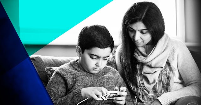 A front-view shot of a mother sitting down on a sofa with her son looking at a mobile phone together