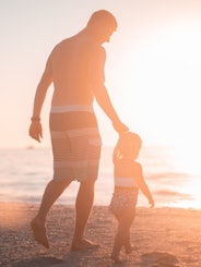 Foster care adoption, man holding child's hand at the beach at sunset
