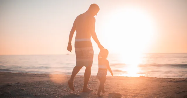 Foster care adoption, man holding child's hand at the beach at sunset