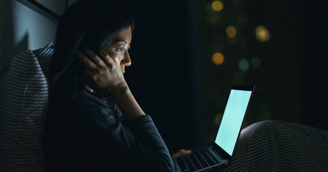 oman in deep thought while using laptop on bed at night