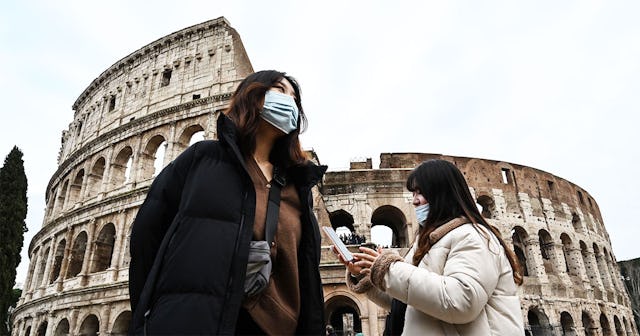 Tourists wearing protective respiratory masks tour outside the Colosseo monument (Colisee, Coliseum)...