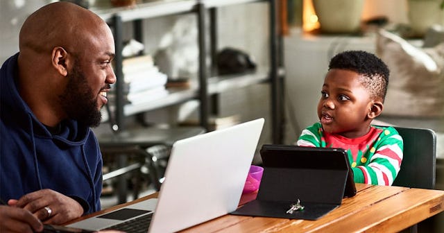 Father and toddler at table with laptop and tablet